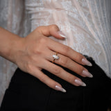 Hand wearing a diamond ring with a blurred lace garment in the background
