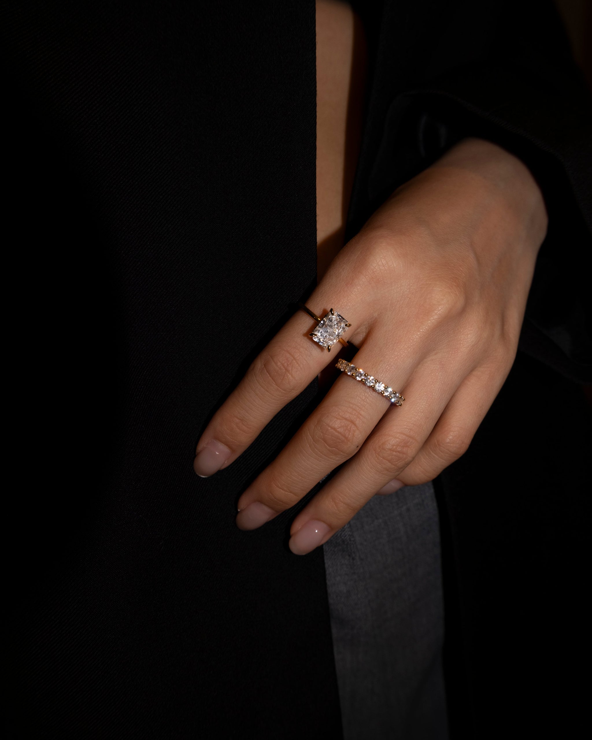 Close-up of a hand wearing the elodie ring and dues ring both in gold on a dark background
