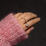Hand wearing a diamond ring with a pink textured sleeve against a dark background