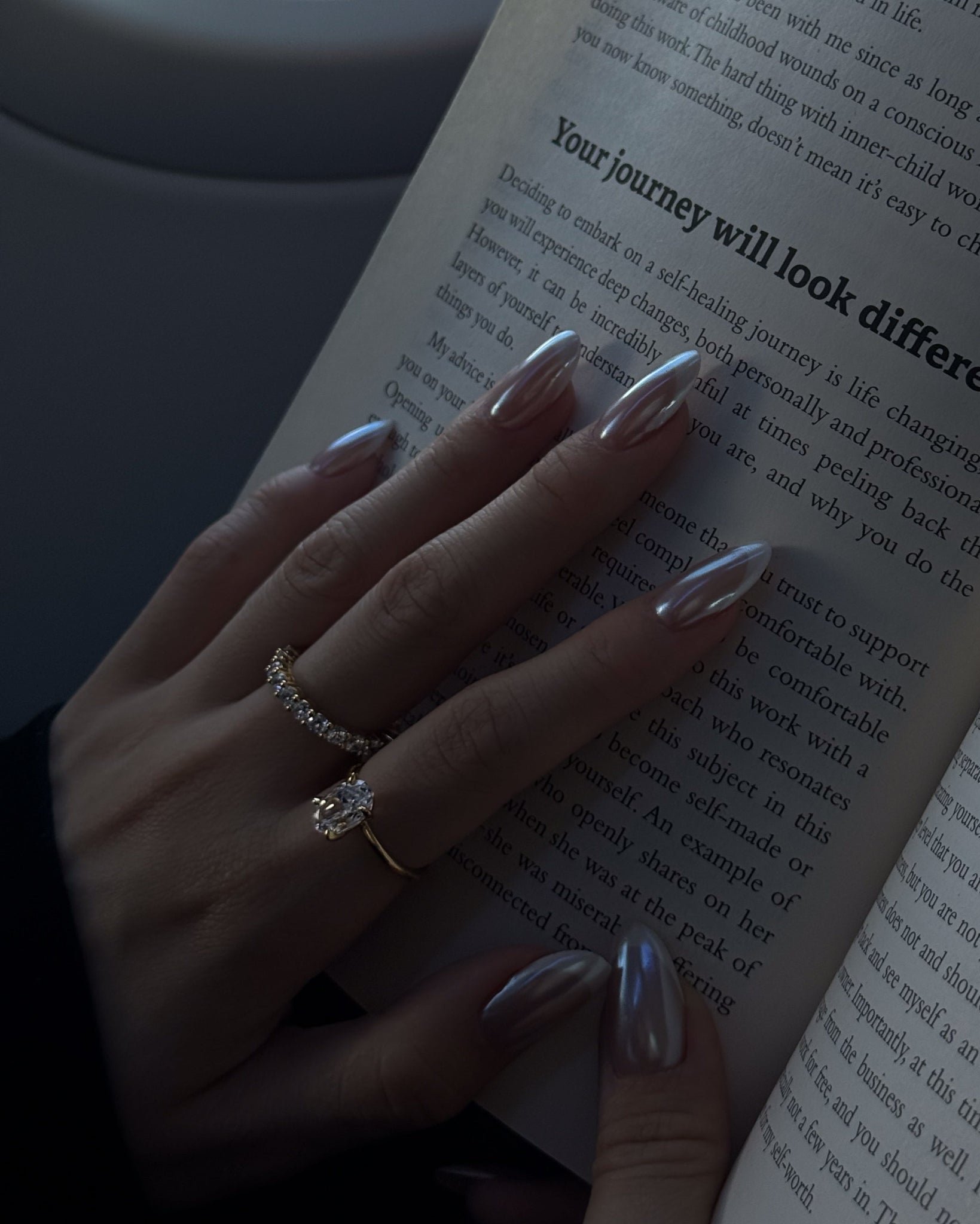 Hand with silver nail polish holding an open book with text.